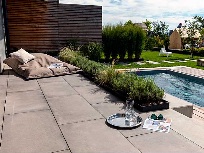 Das Bild zeigt die Terrasse mit Plattenbelag, Poolzugang und Garten